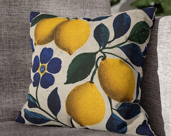 Könnte beinhalten: Quadratisches Kissen mit einem botanischen Design mit gelben Zitronen, blauen Blumen und dunkelgrünen Blättern auf cremefarbenem Hintergrund. Das Kissen liegt auf einem grauen Polstersessel.