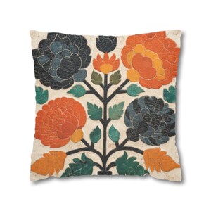 May include: Square decorative pillow with a floral design. The pillow features a cream-colored background with a symmetrical pattern of orange and navy blue flowers, green leaves, and a black stem. The pillow has a soft, textured appearance.