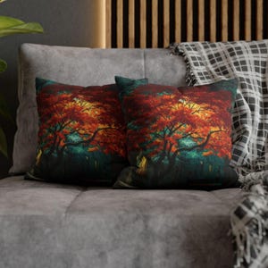 Puede incluir: Dos cojines cuadrados con un diseño vibrante de árbol otoñal. Los cojines presentan una colorida ilustración de un árbol con hojas rojas y naranjas, sobre un fondo verde y amarillo. Los cojines están colocados sobre un sofá gris.