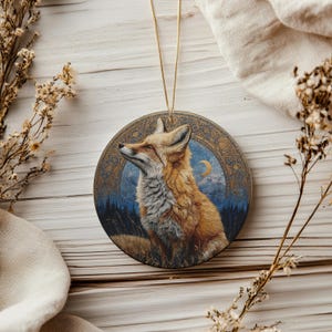 May include: Round ceramic ornament featuring a detailed illustration of a fox with orange and white fur, set against a blue night sky with a crescent moon. The fox is surrounded by a decorative border and a gold hanging string.