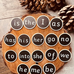 May include: A set of wooden word magnets with black circles and white text. Words include "is", "the", "I", "as", "has", "his", "her", "go", "no", "to", "into", "she", "of", "we", "he", "me", and "be".