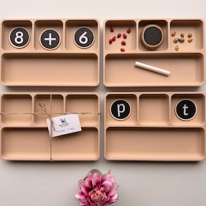 May include: Four light beige rectangular divided trays with multiple compartments. One tray contains circular tokens with the numbers 8, 6, and a plus sign. Another tray holds small ladybug and bee figures, a chalk piece, and a circular chalkboard.