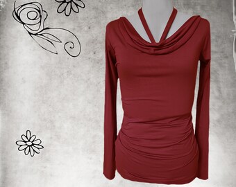 May include: A long-sleeved burgundy top with a cowl neckline and halter-style straps. The top has a fitted silhouette with ruching at the waist. The background is a textured gray with floral doodles.