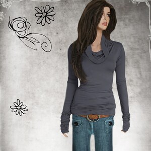 May include: A gray long-sleeved shirt with a cowl neck and thumbholes. The shirt is fitted and has a casual look.