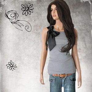 May include: A woman wearing a gray sleeveless top with a black satin bow on the left shoulder. She is also wearing blue jeans with a brown belt.