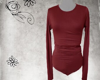 May include: A burgundy long-sleeve bodysuit with a scoop neck. The fitted top has a ruched waist and long sleeves. The background is a mottled gray with black floral line drawings.