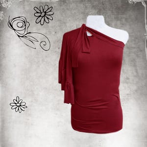 May include: A one-shoulder burgundy top with a ruffle detail on the single sleeve. The top has a knot detail at the neckline.