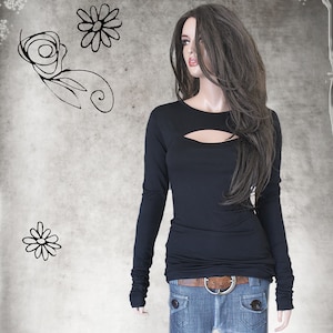 May include: Black long-sleeve top with a keyhole cutout at the chest. The top is paired with blue jeans and a brown belt. The mannequin has long, wavy brown hair. Decorative floral sketches are in the background.