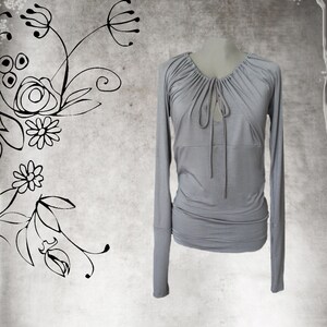 May include: A light gray long-sleeved shirt with a gathered neckline and a tie detail at the front.
