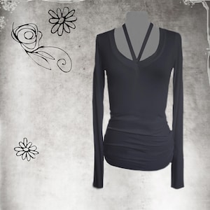 May include: A long-sleeved black top with a V-neck and a unique strap design across the chest. The top features ruching on the side, adding a stylish detail. The background is a textured gray with floral doodles.