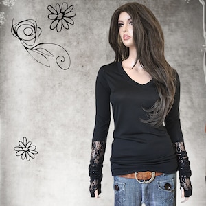May include: A black long-sleeved shirt with a v-neck and lace cuffs. The shirt is worn with blue jeans and a brown belt.