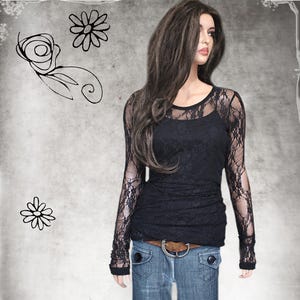 May include: A black long-sleeve top featuring sheer lace sleeves and a solid opaque bodice. The garment is worn with blue denim jeans secured by a brown leather belt with a silver buckle. The design includes a round neckline and fitted cuffs.