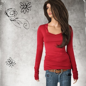 May include: A red long-sleeved shirt with a v-neck and cuffed sleeves. The shirt is fitted and has a slightly gathered look at the waist. The model is wearing blue jeans with a brown belt.