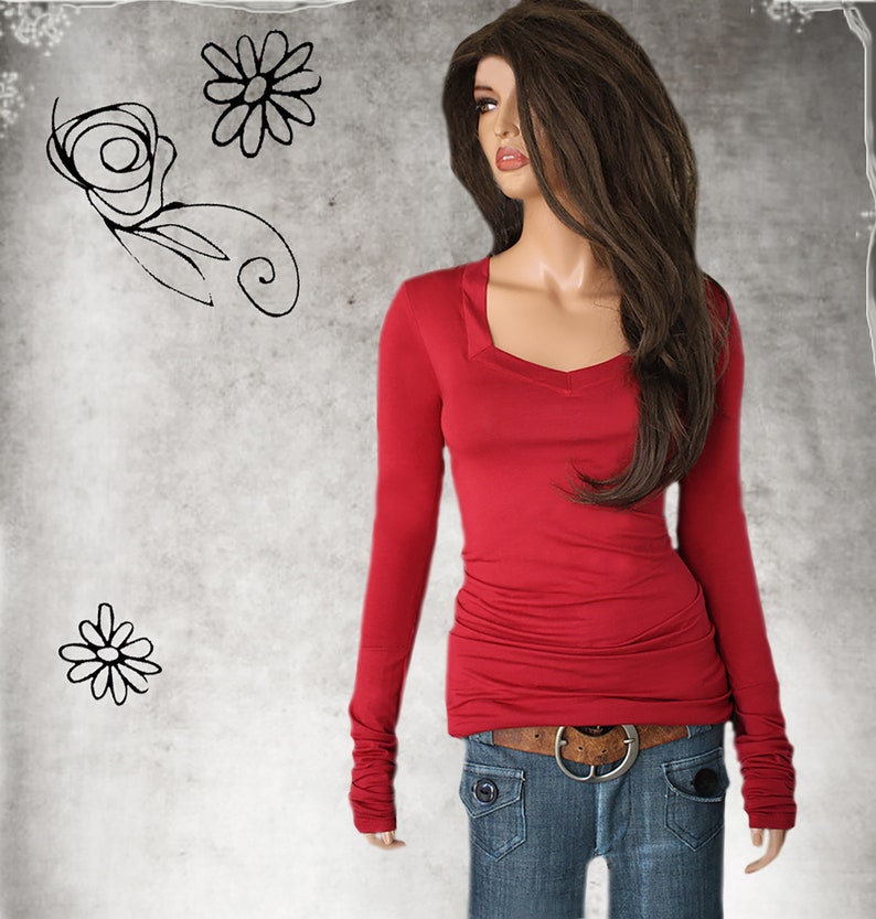 May include: A red long-sleeved shirt with a v-neck and cuffed sleeves. The shirt is fitted and has a slightly gathered look at the waist. The model is wearing blue jeans with a brown belt.