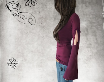 May include: A long-sleeved, deep purple top with flared sleeves and cut-out details. The top is paired with blue jeans. The background features floral doodles in black against a textured gray backdrop. The overall aesthetic is casual and artistic.