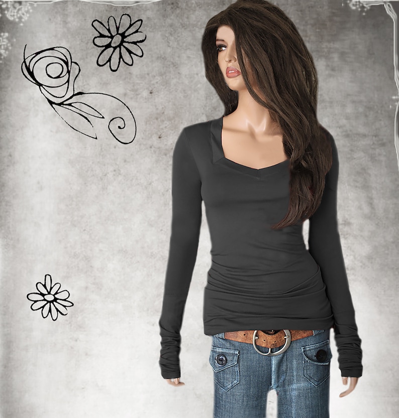 May include: A charcoal gray long-sleeved shirt with a scoop neck and cuffed sleeves. The shirt is fitted and has a slightly gathered look at the waist. The model is wearing the shirt with blue jeans and a brown belt.