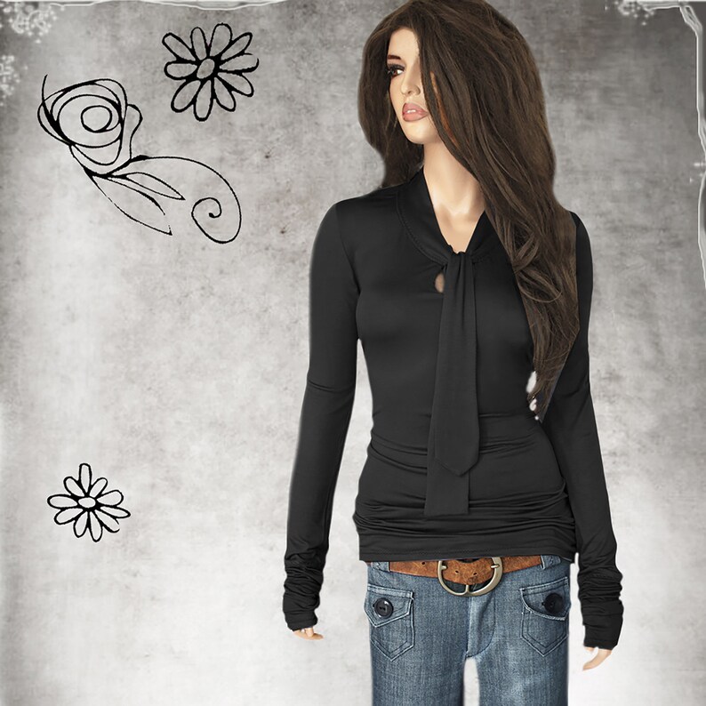 May include: A black long-sleeved shirt with a tie at the neck. The shirt has a fitted silhouette and is made of a soft, stretchy fabric. The model is wearing the shirt with blue jeans and a brown belt.