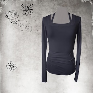 May include: A dark navy blue long-sleeve shirt with a square neckline and a fitted silhouette. The shirt has a unique strap detail at the shoulders and subtle ruching at the waist. The background is a textured gray with floral doodles.