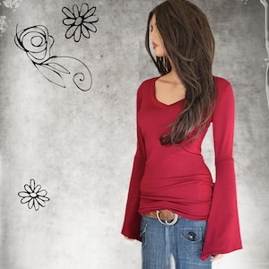 May include: A burgundy long-sleeve top with a V-neck and flared sleeves. The top is paired with blue jeans and a brown belt with a silver buckle. The background features floral sketches.