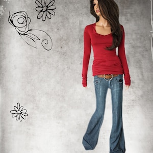 May include: A woman wearing a red long-sleeved shirt with a v-neck and a pair of blue jeans with a brown belt.