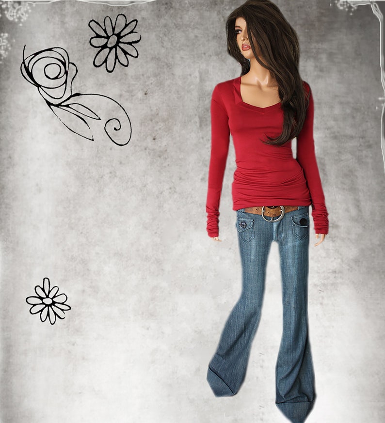 May include: A woman wearing a red long-sleeved shirt with a v-neck and a pair of blue jeans with a brown belt.
