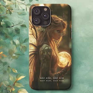 Puede incluir: Funda de teléfono con un diseño de arte fantástico. Muestra a una mujer con alas de hada sosteniendo un orbe brillante. El texto "HALF WILD, HALF WISH" está impreso en la parte inferior. La funda tiene un módulo de cámara negro.