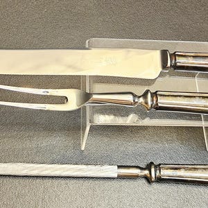 Pu&ograve; includere: Un set da intaglio in tre pezzi con manici argentati e lame in acciaio inossidabile. Il set comprende un coltello da intaglio, una forchetta da intaglio e un'acciarino. I manici hanno un design decorativo e scanalato.