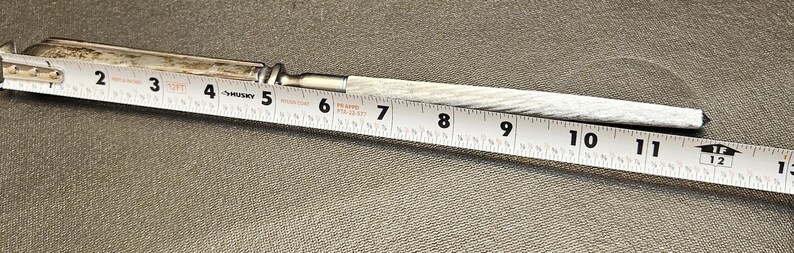 Pu&ograve; includere: Un coltello antico argentato con un manico strutturato, lungo circa 30 cm. Un metro a nastro bianco &egrave; posto accanto al coltello, mostrandone la lunghezza.