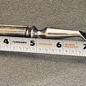 Pu&ograve; includere: Una forchetta da intaglio color argento con due rebbi, lunga circa 25 cm. L'impugnatura ha un design ornato. La forchetta &egrave; posizionata accanto a un metro a nastro.