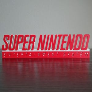 May include: A red and white Super Nintendo Entertainment System sign. The words "SUPER NINTENDO" are in bold, red letters above the words "ENTERTAINMENT SYSTEM" in smaller, red letters.