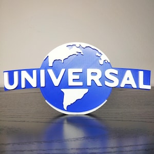 May include: A blue and white Universal logo, featuring a globe and the word "UNIVERSAL" in white block letters. The logo is set against a dark surface, with a light gray background.