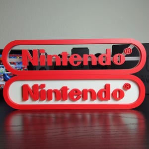 May include: Two red and white Nintendo logos, one stacked above the other. The top logo is a red outline with the word "Nintendo" in red. The bottom logo is a red outline with a white interior and the word "Nintendo" in red.