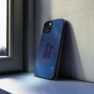 May include: A black phone case with a blue starry sky design. The case features a silhouette of two figures connected by a red string, with Japanese text below. The case is leaning against a white wall.