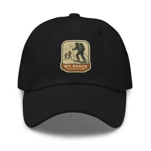 May include: Black baseball cap featuring an embroidered patch with a skier on skis and the text "MT. BAKER WASHINGTON". The patch has a vintage, outdoorsy aesthetic with brown, beige, and green tones. The cap has a curved brim and a structured fit.