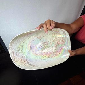 May include: An oval glass bowl featuring a white base with an iridescent, pearlescent finish and a swirling, speckled pattern in soft pastel tones of pink, blue, and green that creates a shimmering, multi-colored effect across the interior surface.