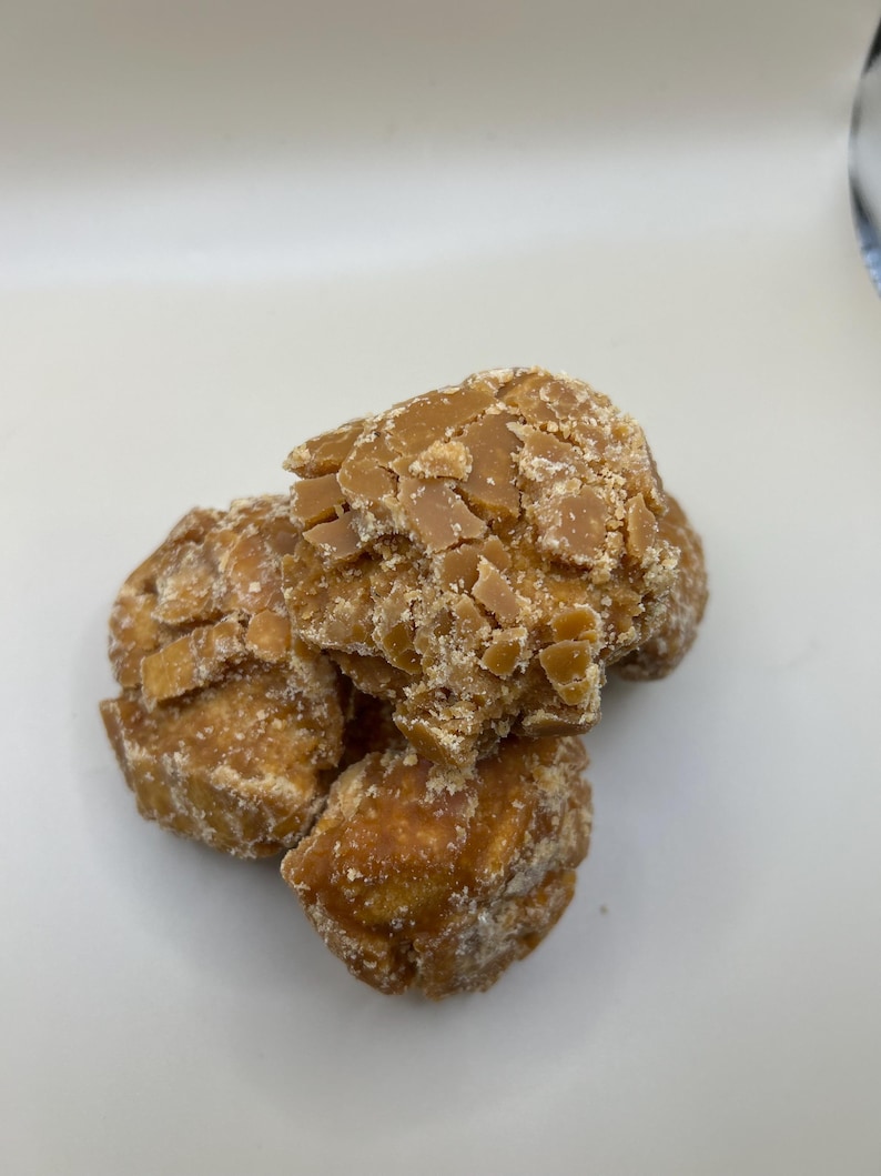 May include: A close-up shot of several pieces of brown, textured candy. The candy has a rough, uneven surface with a light-colored, crystalline coating. The pieces are clustered together, suggesting a snack or treat.