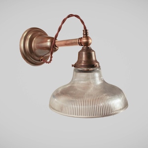 May include: Vintage-style wall sconce with a clear, ribbed glass shade and a copper-toned metal fixture. The fixture includes a round wall mount, a curved arm, and a decorative bulb holder. The wiring is a twisted brown cord.