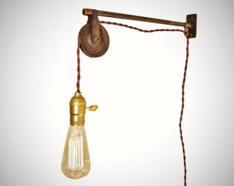 May include: A rustic industrial style wall sconce with a pulley system and a single exposed bulb. The sconce is made of metal and has a brown finish. The cord is brown and the bulb is clear glass.