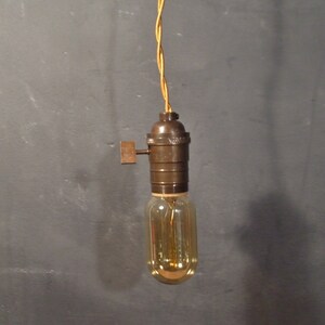 May include: A vintage-style pendant light with a brown metal socket and a clear glass bulb. The light is hanging from a yellow braided cord.