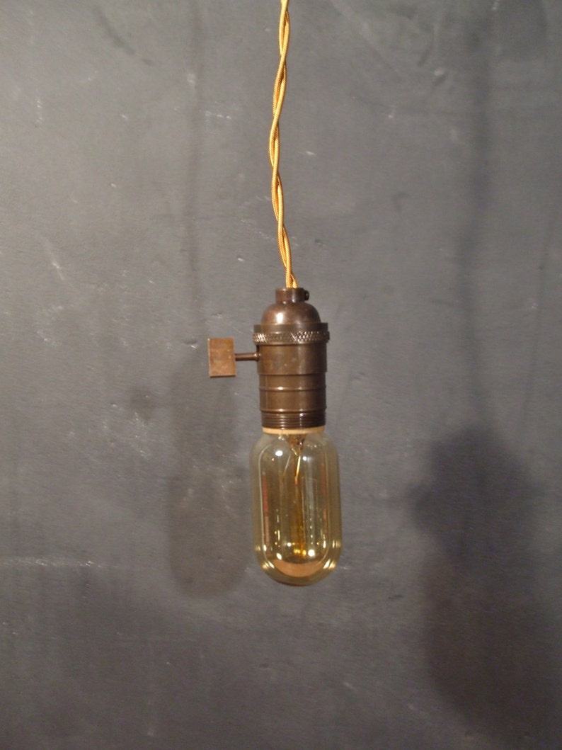 May include: A vintage-style pendant light with a brown metal socket and a clear glass bulb. The light is hanging from a yellow braided cord.
