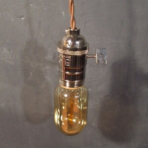 May include: A chrome light fixture with a brown cord and a clear glass bulb. The bulb has a warm, amber glow.