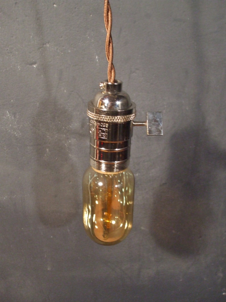 May include: A chrome light fixture with a brown cord and a clear glass bulb. The bulb has a warm, amber glow.