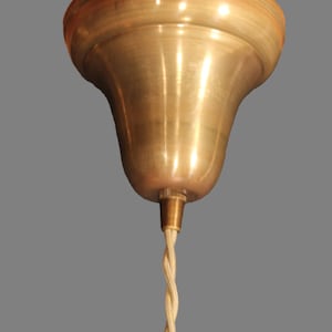 Puede incluir: Una lámpara de techo de latón con una cubierta en forma de campana y un cable beige trenzado.