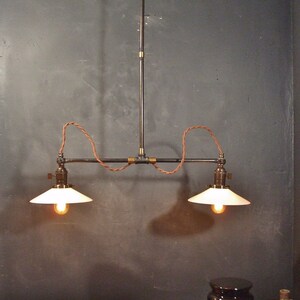 May include: A two-light industrial style pendant light fixture with black metal pipes and white glass shades. The fixture is suspended from the ceiling with a black cord and has a brass accent.