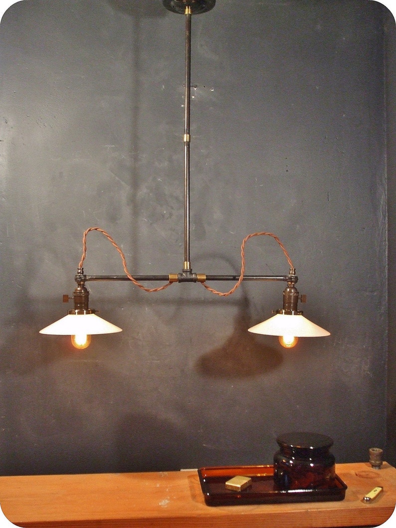 May include: A two-light industrial style pendant light fixture with black metal pipes and white glass shades. The fixture is suspended from the ceiling with a black cord and has a brass accent.