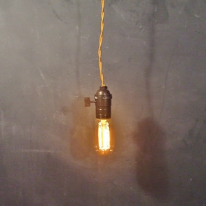 May include: A single light bulb hanging from a yellow cord against a gray wall. The light bulb is on and glowing.