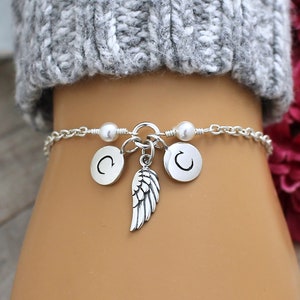 May include: A silver chain bracelet with two silver charms that say "C" and a silver angel wing charm.