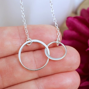 May include: A silver necklace with two interlocking circles. The circles are smooth and shiny, and the necklace is delicate and feminine.