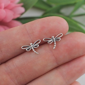 May include: A pair of silver dragonfly earrings. The earrings are small and delicate, and they feature a detailed dragonfly design.