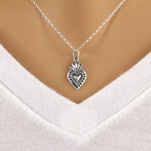 May include: A silver necklace with a heart-shaped pendant. The pendant has a detailed design with a smaller heart in the center.